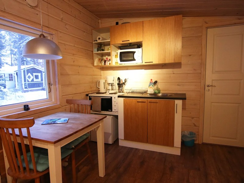 Cozy wooden kitchen with dining table, chairs, microwave, and window showing snowy landscape.