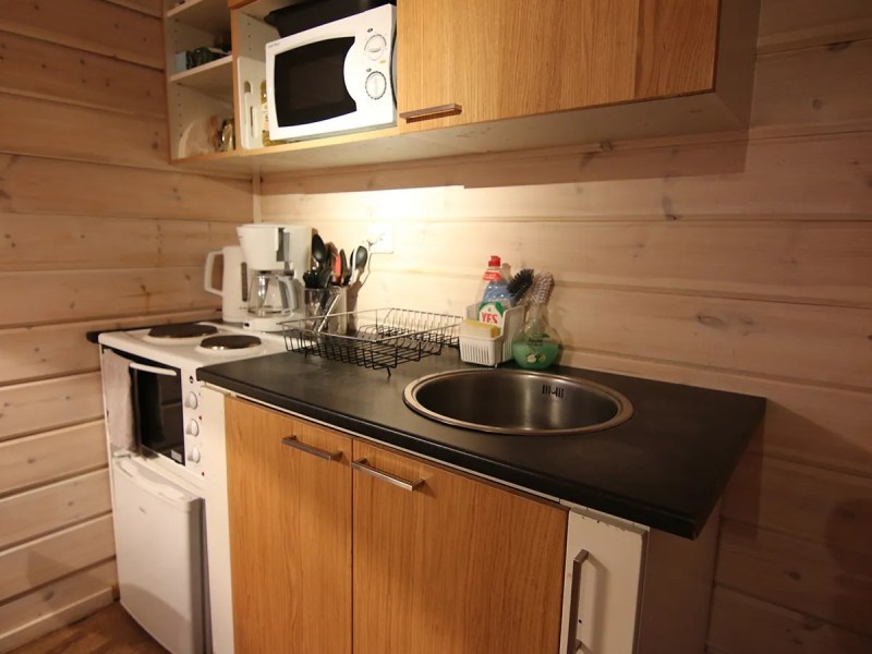 Compact kitchen with wooden cabinets, stove, microwave, and a sink on a black countertop.