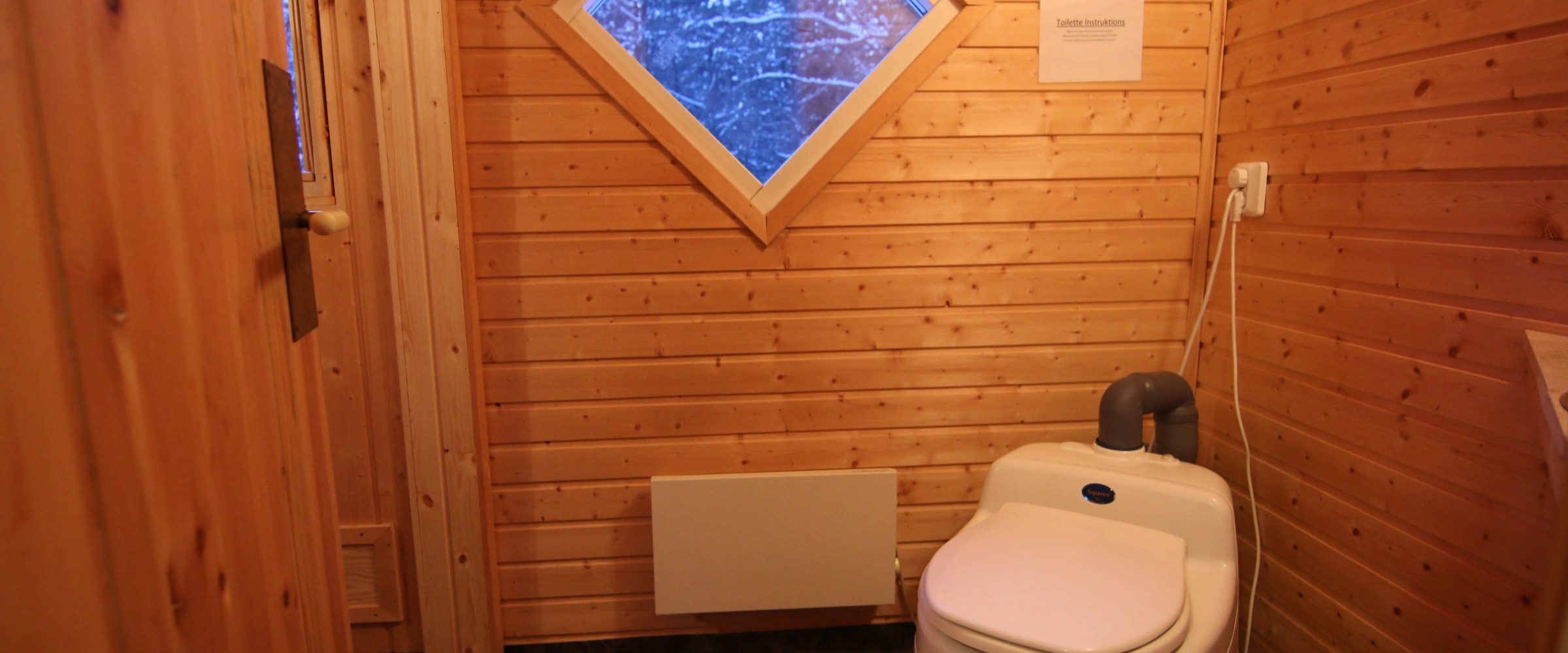 Wood-paneled bathroom with a composting toilet and diamond window.