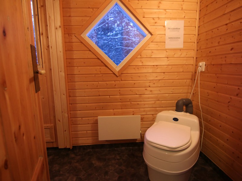 Wood-paneled bathroom with a composting toilet and diamond window.