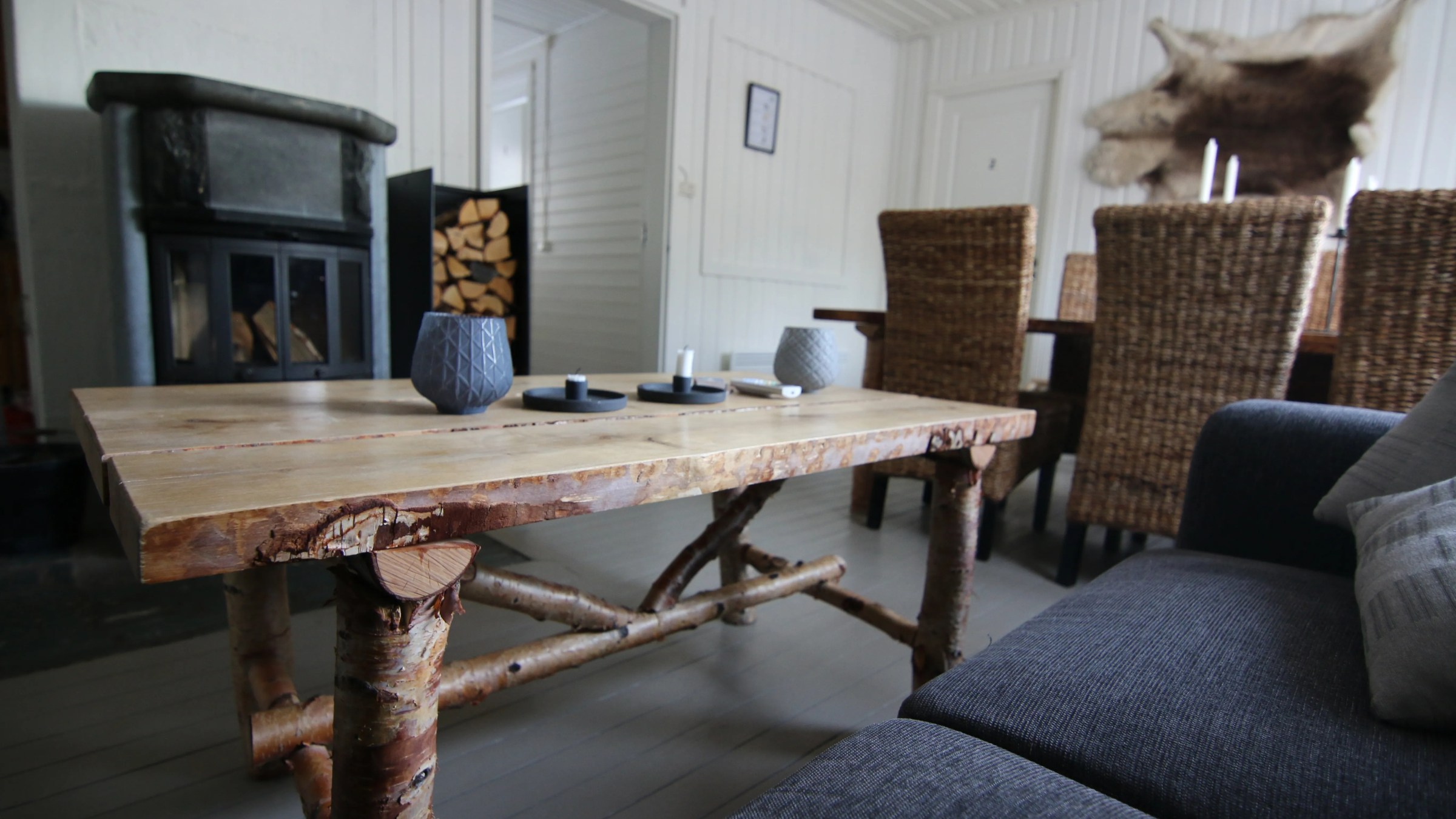 Rustic living room with wooden table, wicker chairs, and stone fireplace.