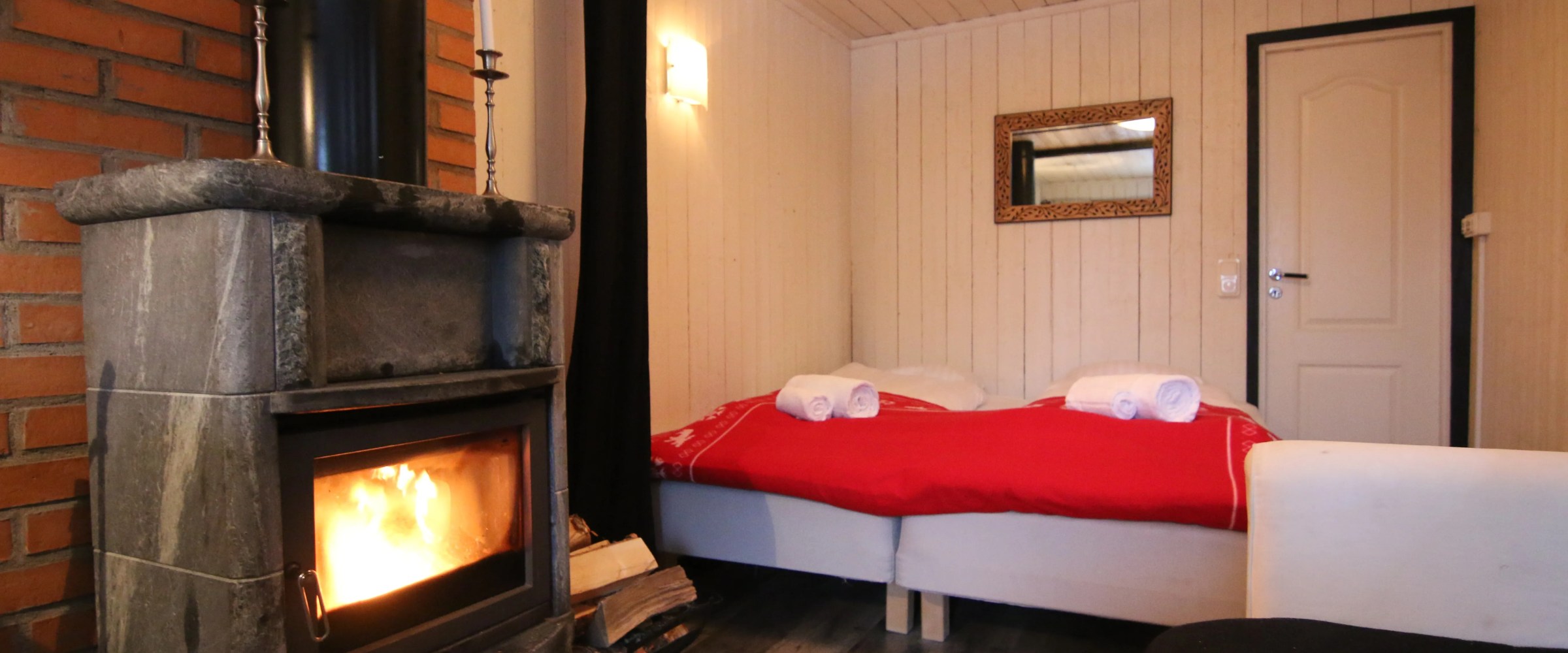 Cozy bedroom with a lit stone fireplace, red bed cover and towels, and a wall mirror.