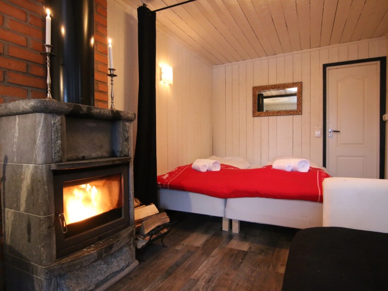 Cozy bedroom with a lit stone fireplace, red bed cover and towels, and a wall mirror.