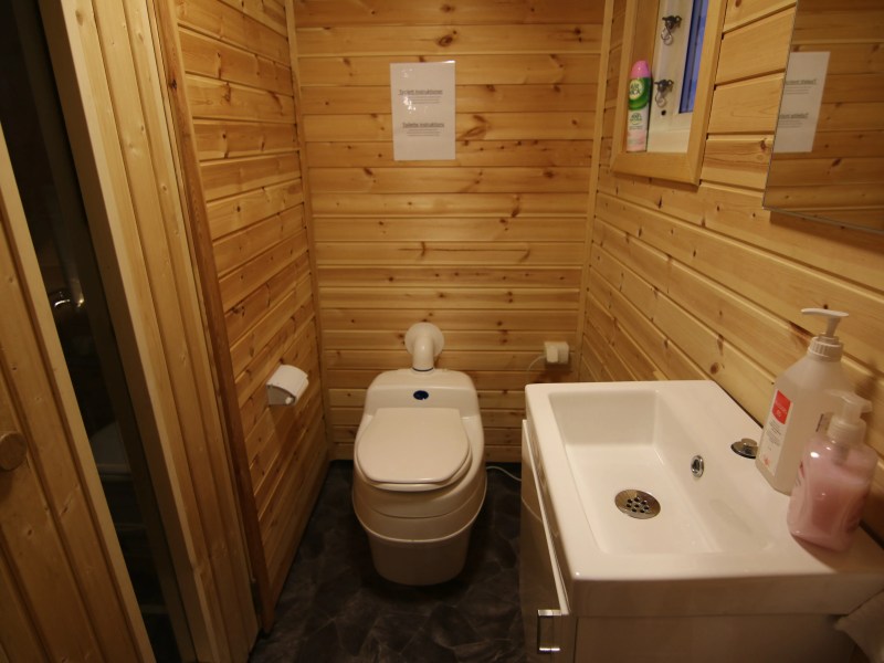 Wood-paneled bathroom with a composting toilet and small sink.