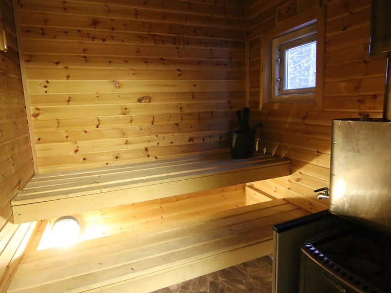 Wooden sauna interior with benches, a window, and a metal stove in the corner.