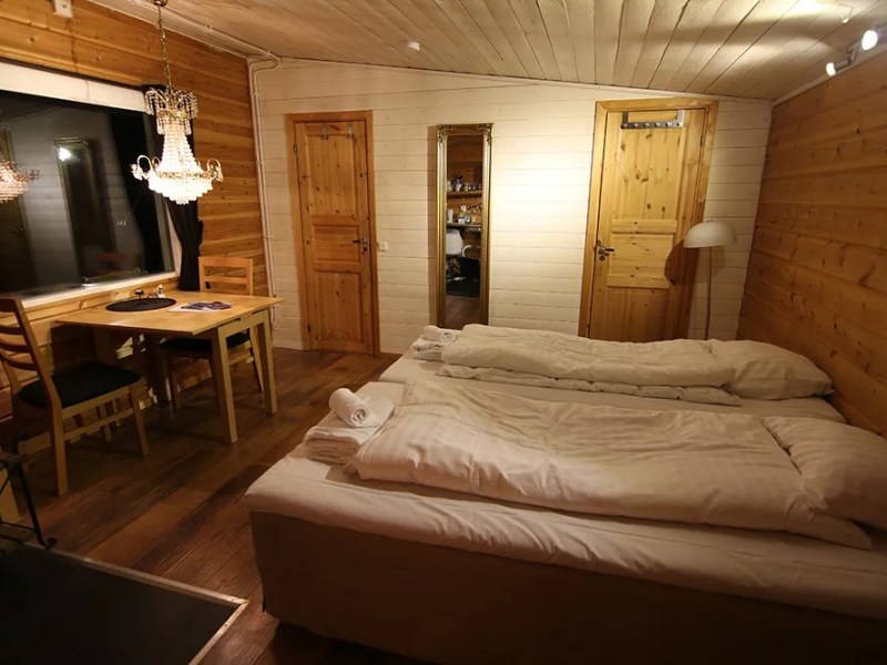 Cozy wooden room with two beds, dining table, chandelier, and a mirror between two doors.