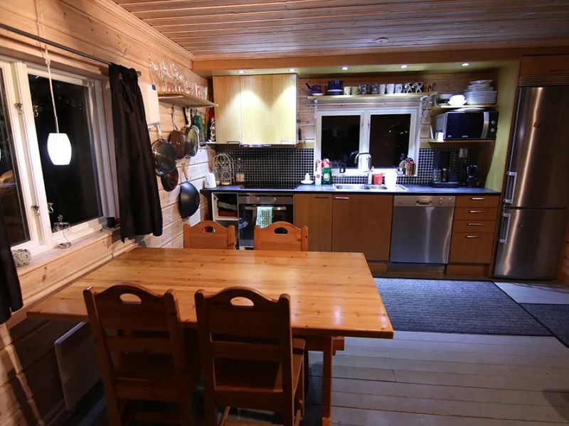 A cozy kitchen with wooden dining table, chairs, and modern appliances against log cabin walls.