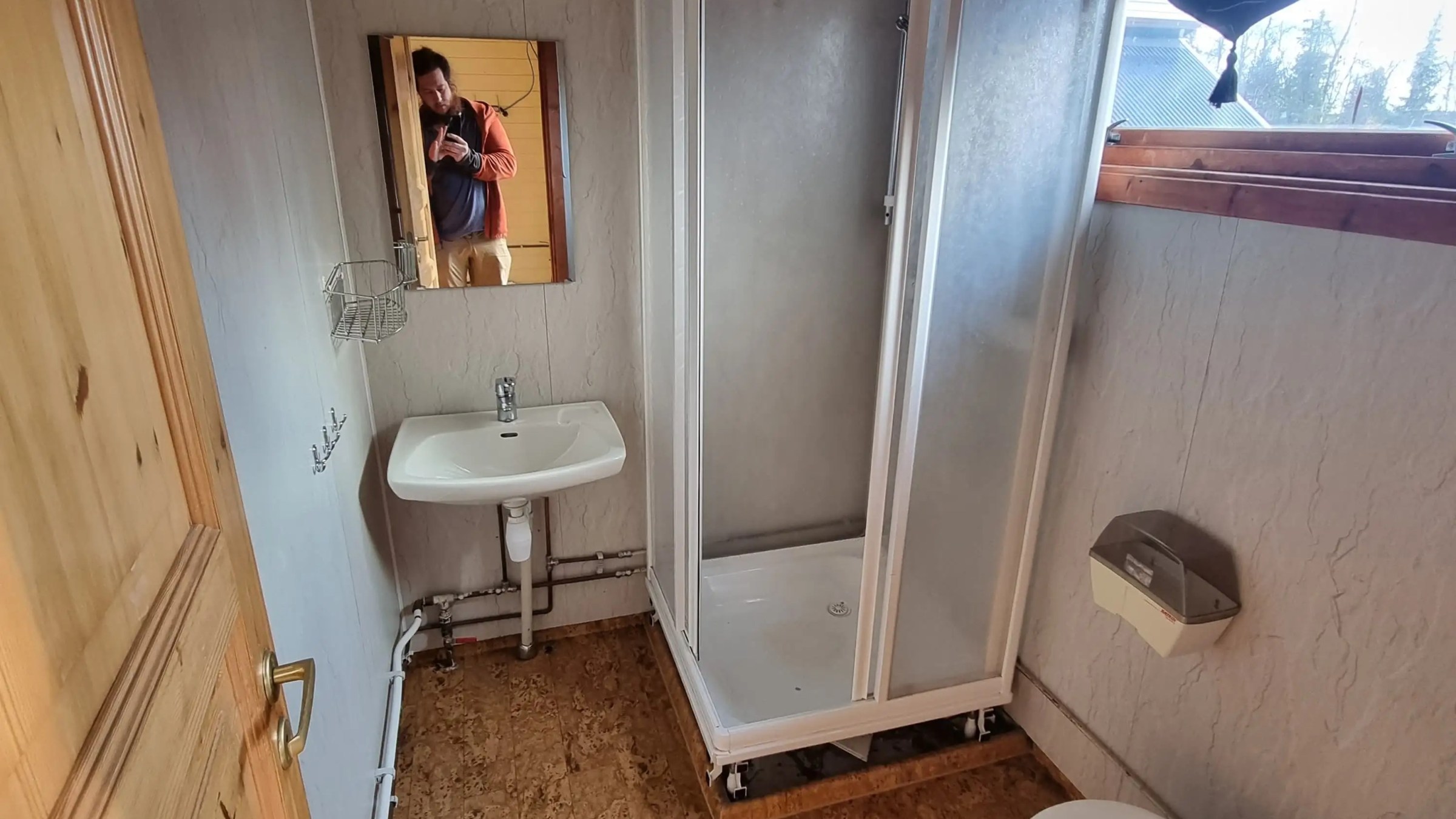 Small bathroom with shower, sink, toilet, and mirror. Wooden ceiling and window with view.