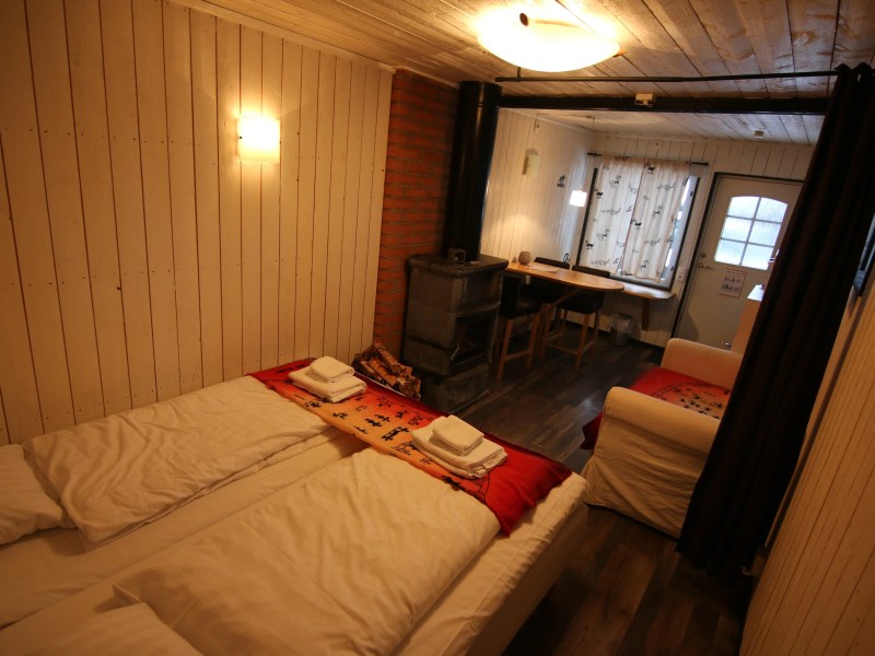 Cozy room with twin beds, a wood stove, and a small dining area near a window.