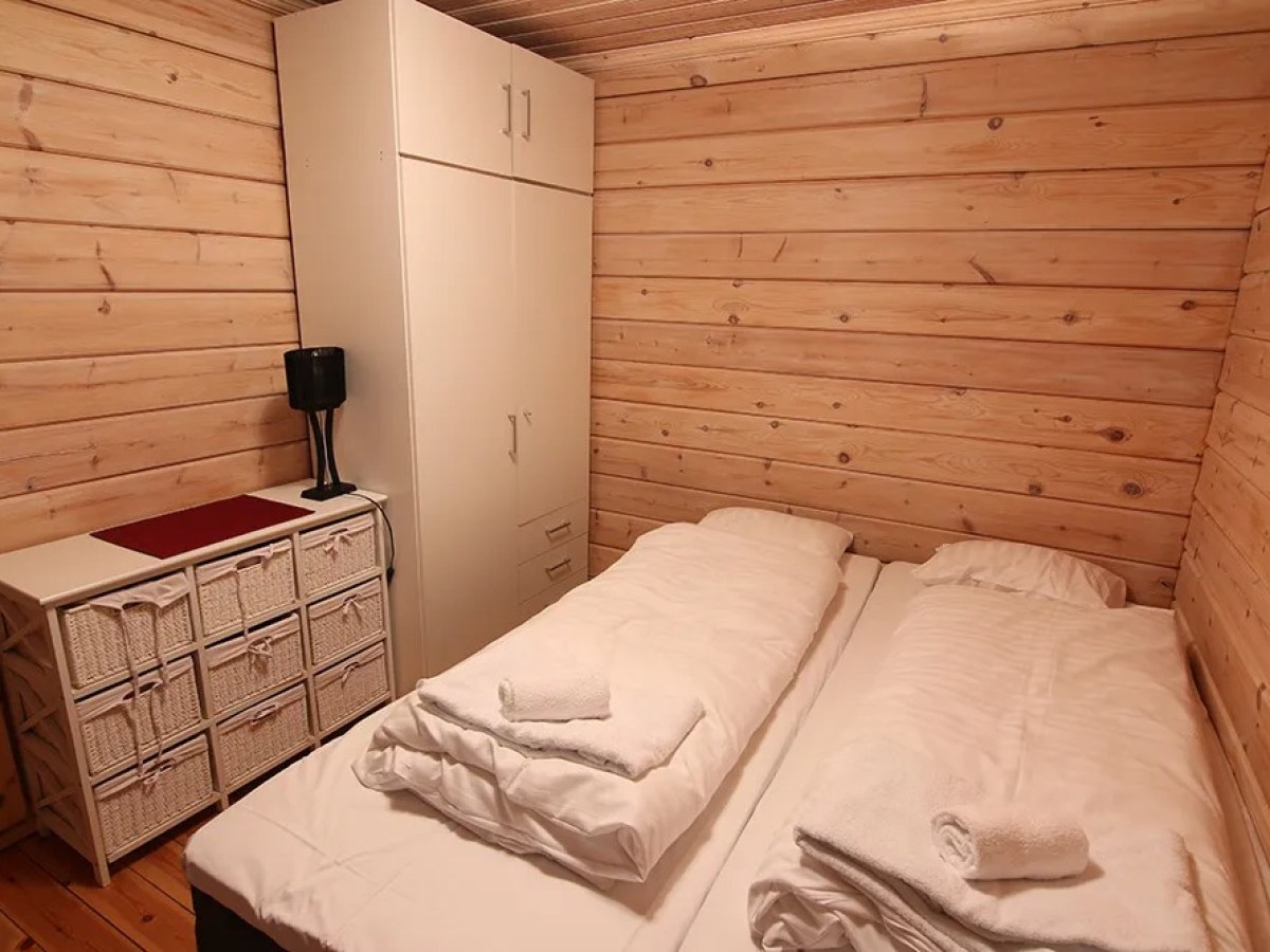 Cozy wooden bedroom with twin beds, white wardrobe, drawers, and a lamp.