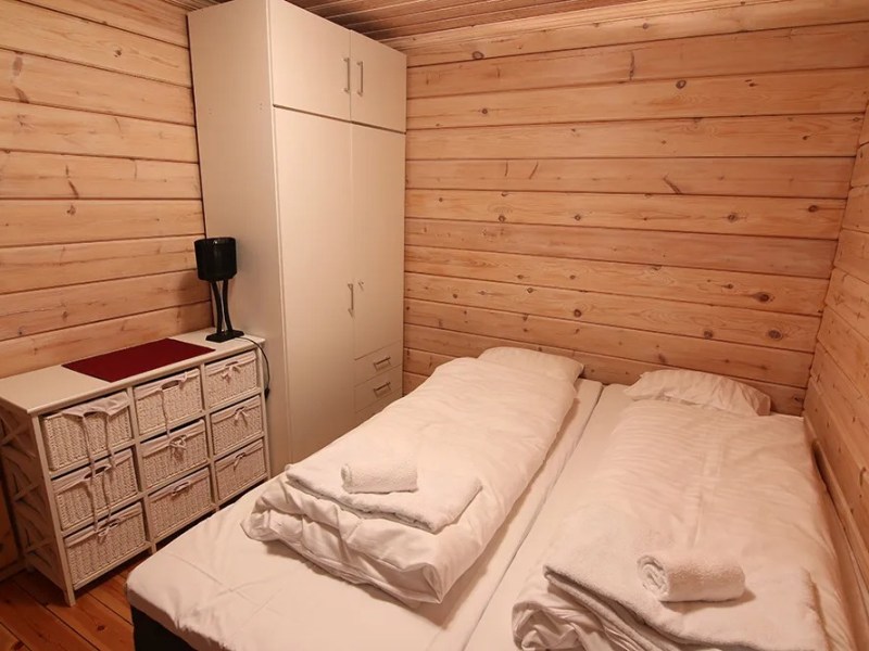 Cozy wooden bedroom with twin beds, white wardrobe, drawers, and a lamp.