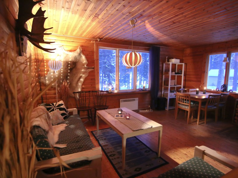 Cozy wooden cabin interior with sofa, table, dining area, and warm lighting.