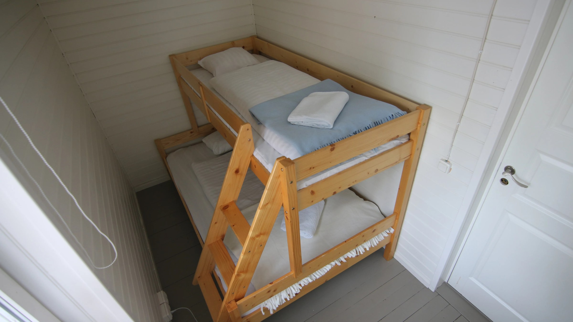 Small room with wooden bunk bed and white bedding, white walls, and a closed door.