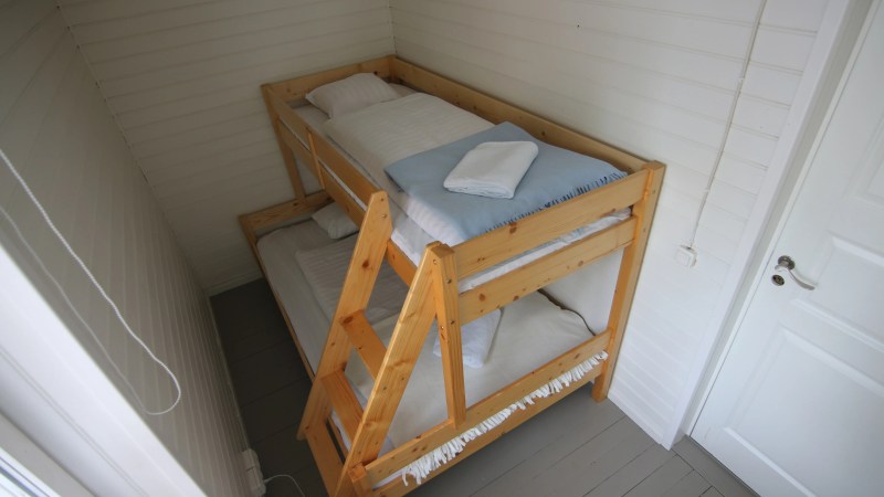 Small room with wooden bunk bed and white bedding, white walls, and a closed door.