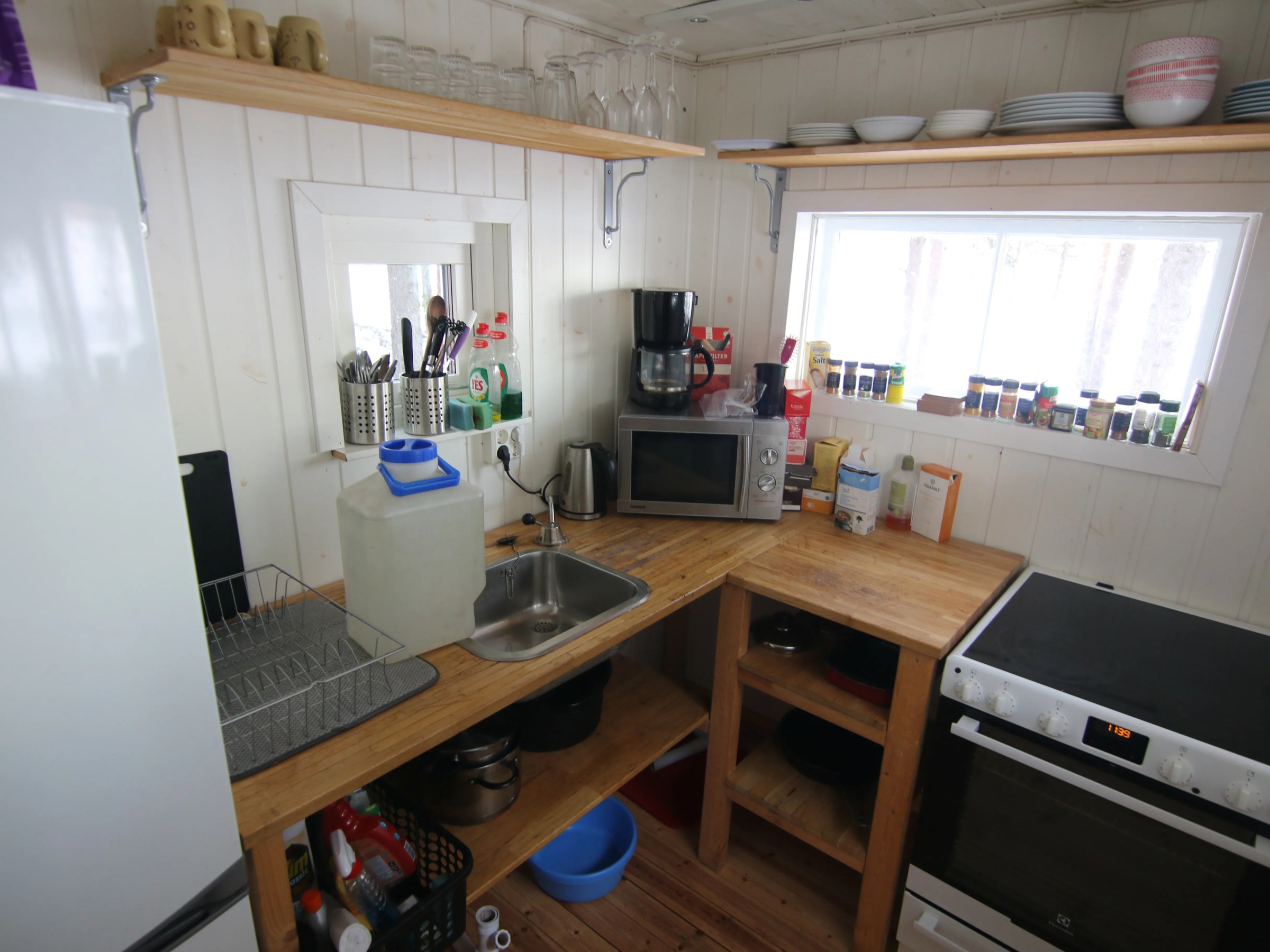 Small kitchen with wooden countertops, sink, microwave, stove, and shelves with dishes and spices.