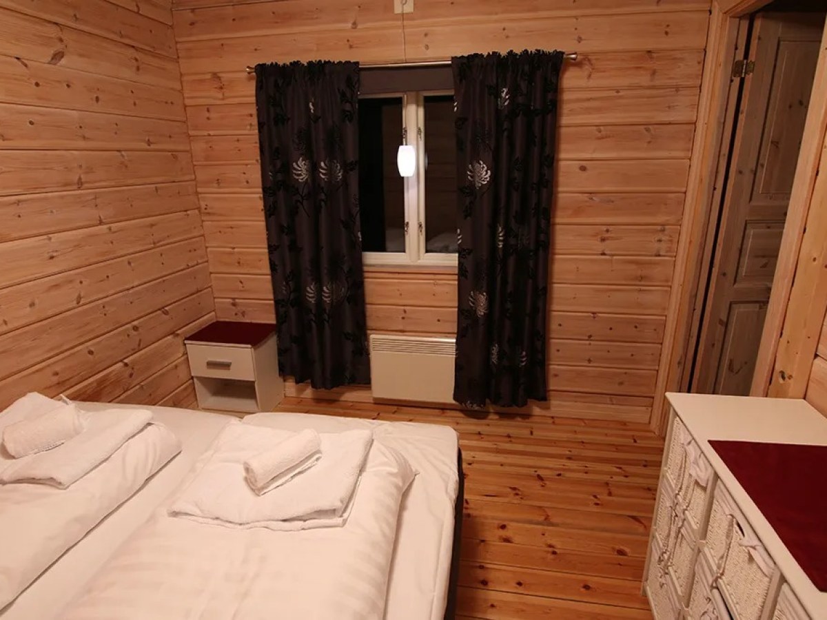 Wood-paneled bedroom with two beds, dark curtains, and a nightstand near a window.