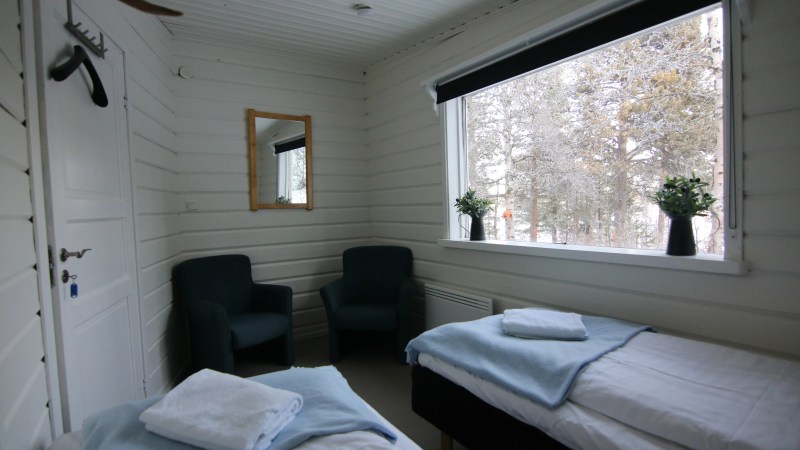 Small room with two single beds, two chairs, a window view, and wall-mounted mirror.