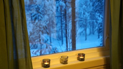 Snowy trees seen through window with green curtains and candles on sill.