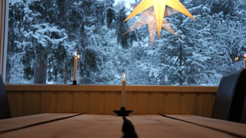 Candles on table with snowy tree view and glowing star decoration in window.