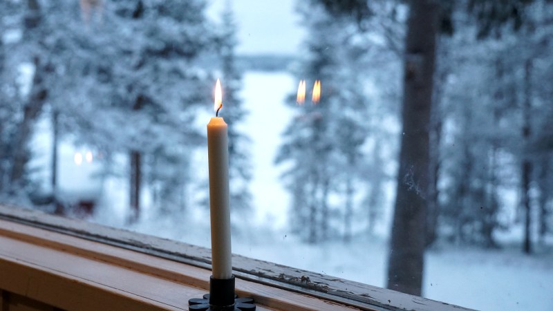 Lit candle on a windowsill with snowy trees visible outside.