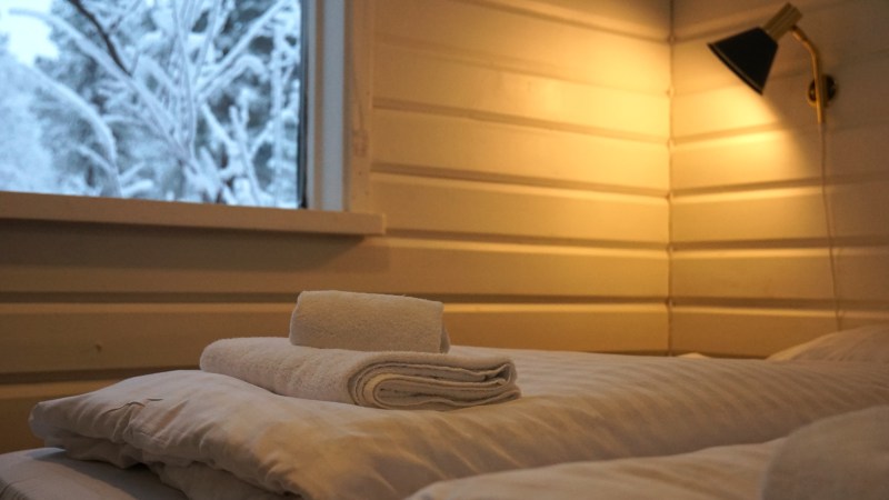 Cozy bedroom with soft lighting, a neatly made bed with towels, and a snowy view outside the window.