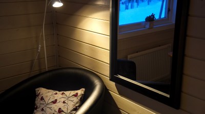 Cozy room corner with chair, pillow, mirror, lamp, and window view.