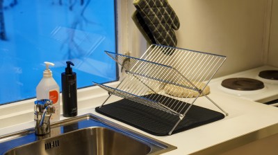 Kitchen sink with soap bottles, dish rack, and window with blue sky view.