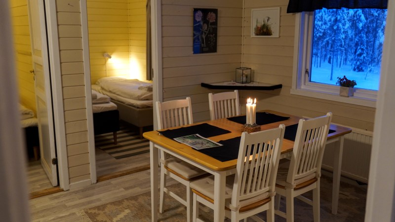 Cozy dining area with candles on table, adjacent to bedroom with twin beds, window view of snowy forest.