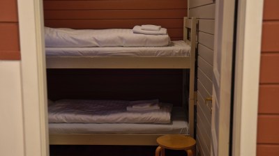 Bunk bed in a small room with folded towels on each bed and a wooden stool nearby.