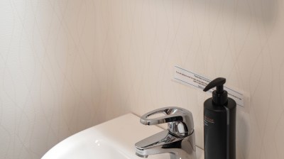 Small bathroom sink with chrome faucet and black soap dispenser on a white counter.