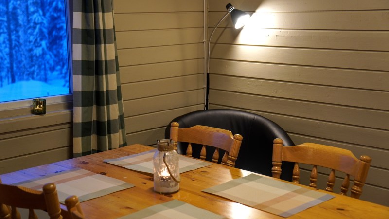 Cozy dining area with wooden table, chairs, and lit lamp. Window shows snowy trees.