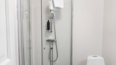 Modern glass shower enclosure with towel and bottle inside a white-tiled bathroom.