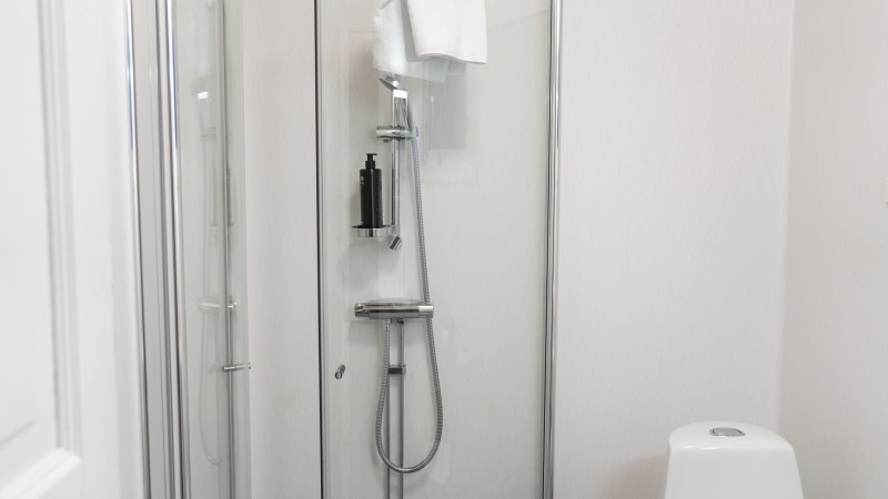 Modern glass shower enclosure with towel and bottle inside a white-tiled bathroom.