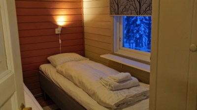 Cozy room with a single bed, wall lamp, wintery window view, and folded towels on the bed.