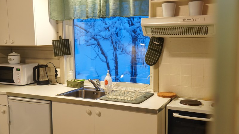 Cozy kitchen with green curtains, a window view of snowy trees, and various kitchen appliances.