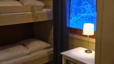 Bunk beds with white bedding beside a lit lamp on a table, with snowy view through window.