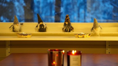 Four gnome figurines sit on a windowsill with two candles in front, with a snowy landscape outside.