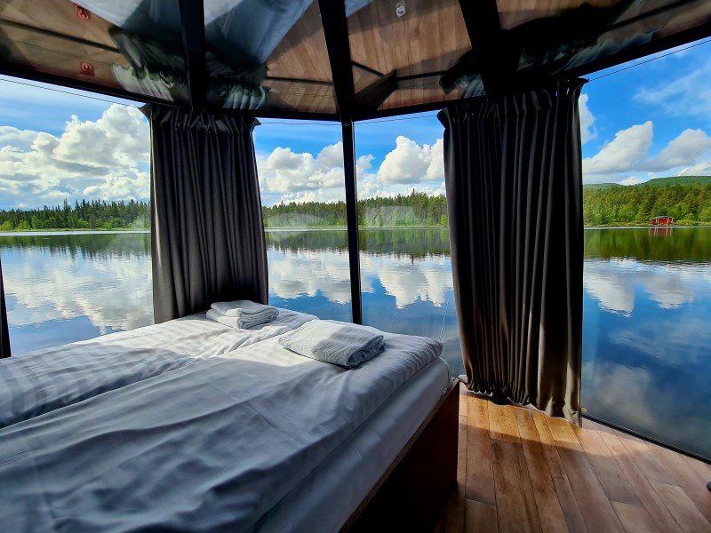 Bedroom with panoramic lake view, large windows, and folded towels on a neatly made bed.
