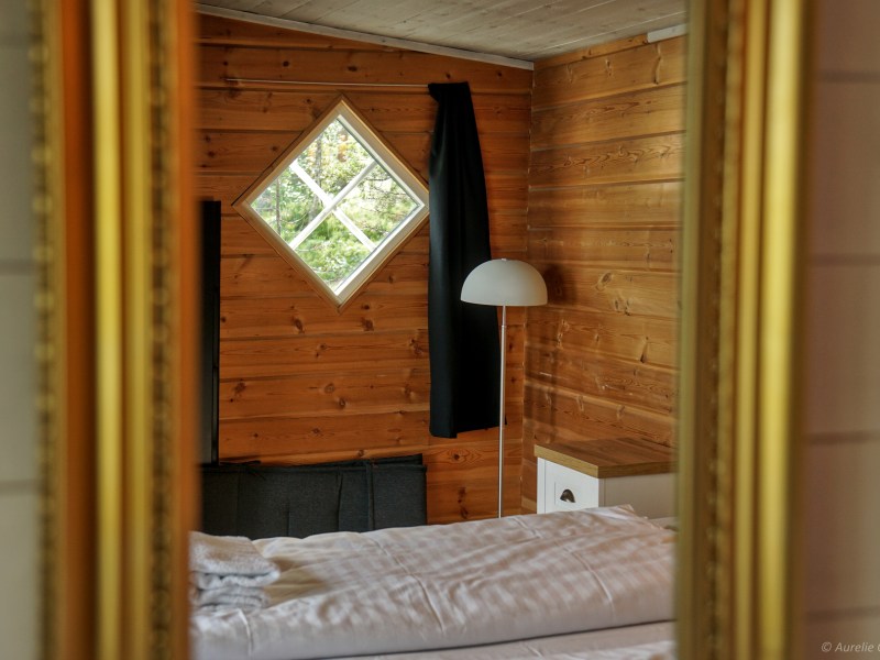 Reflection of a cozy wooden room with a bed, lamp, and diamond window.