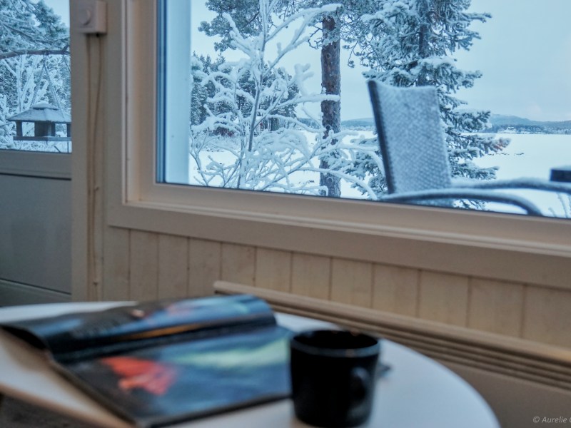 Cozy room view of snowy landscape with table, open magazine, and cup.