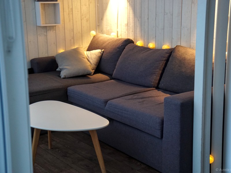 Cozy living room with a dark sofa, pillows, white table, and string lights.