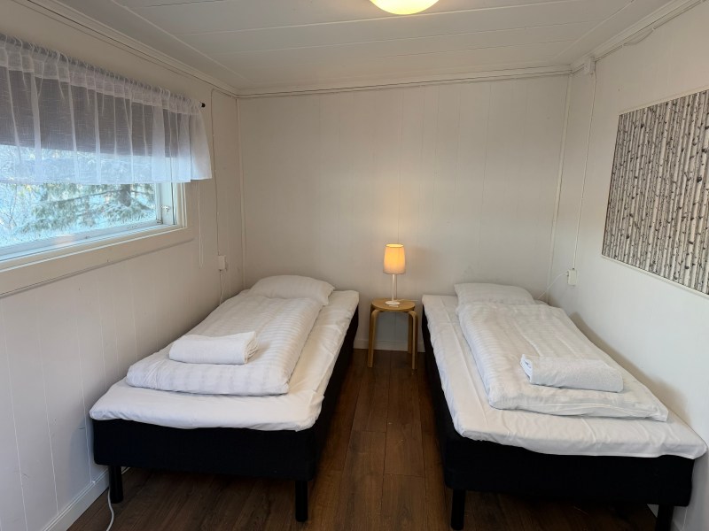 Two single beds with white linens in a small room; a lamp on a table between them.