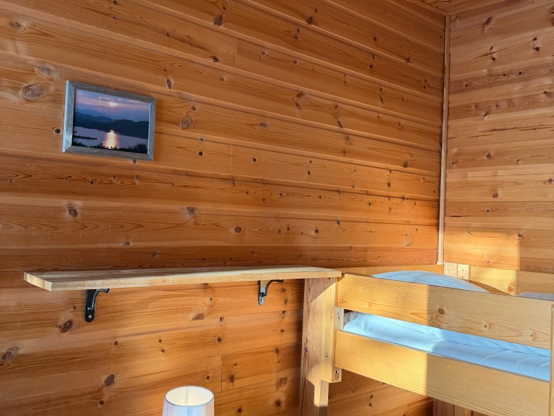 Wood-paneled room with bunk beds, wall shelf, table lamp, and small landscape photo.