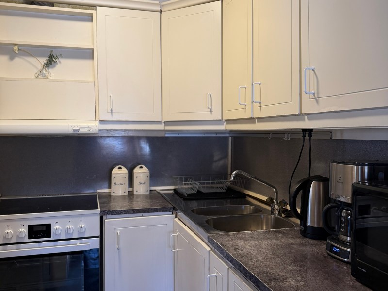Compact kitchen with white cabinets, oven, sink, and countertop appliances including a kettle and toaster.