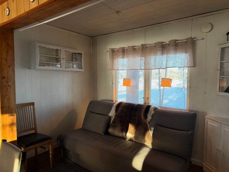 Cozy room with a sofa, fur throw, chair, cabinet, and window with sheer curtains.