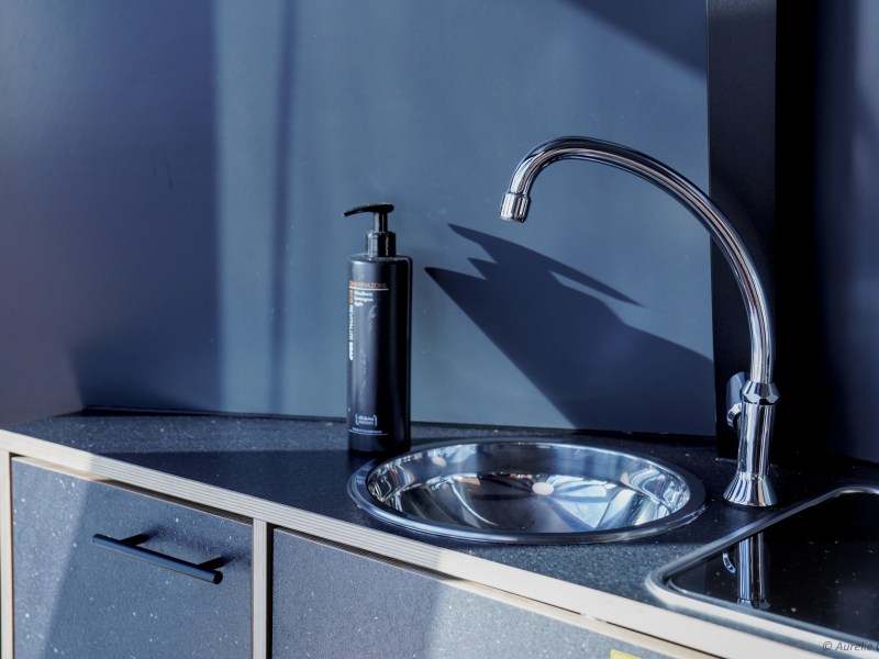 Shiny metal faucet over sink with soap dispenser on dark countertop.