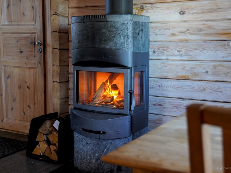 Cozy cabin interior with a wood-burning stove and a stack of firewood nearby.