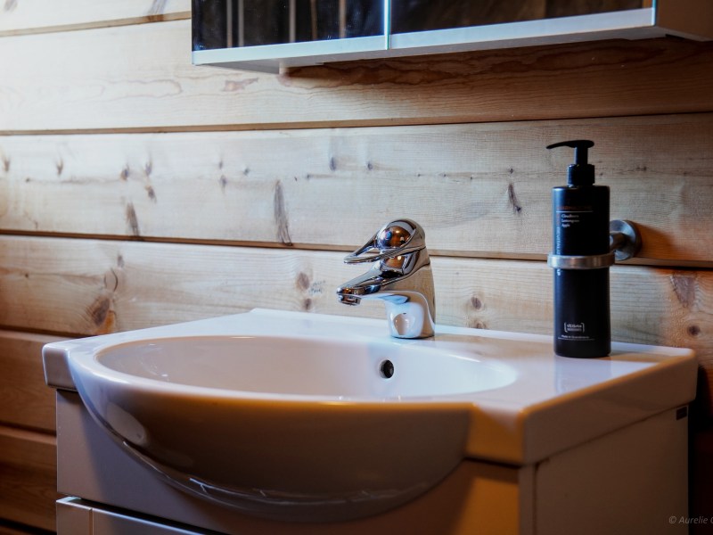 Bathroom sink with chrome faucet and soap dispenser on wooden wall background.