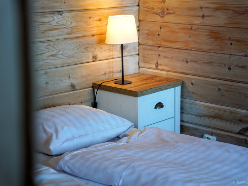 Cozy bedroom with wooden walls, white bedding, and a bedside lamp on a nightstand.