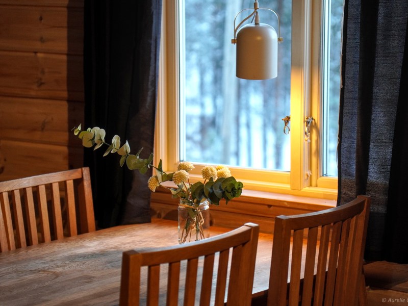 Cozy wooden dining table with flowers by a window, soft indoor lighting.